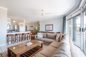 Una sala de estar moderna con sofá, mesa de centro y un comedor con taburetes de bar.