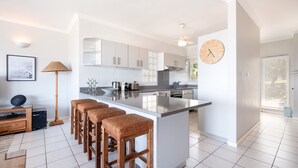 A modern kitchen with a large island, bar stools, and a clock on the wall. - Barrington 116 (Ballito)
