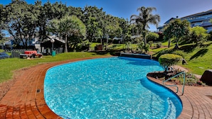 A swimming pool with a brick deck, surrounded by greenery and a building in the background. - Barrington 116 (Ballito)