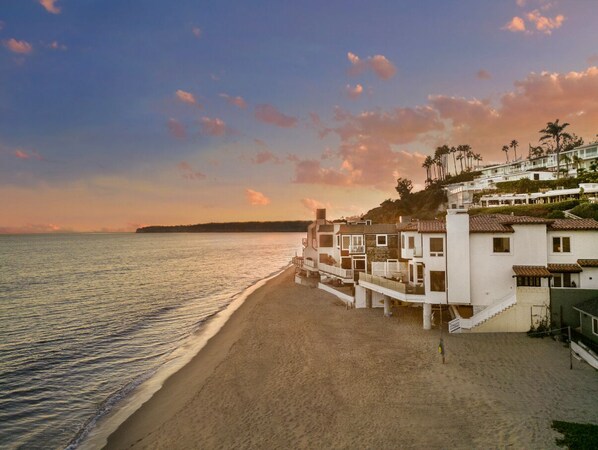 Un hotel frente a la playa con varias construcciones, una playa de arena y una vista despejada del océano.