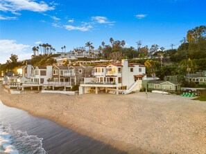 Una propiedad frente a la playa con varias edificaciones, incluyendo una casa grande con balcón y una estructura más pequeña con techo.