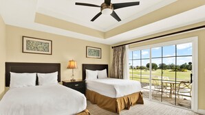 A hotel room with two beds, a ceiling fan, a view of a golf course through a sliding glass door, and a framed picture on the wall.