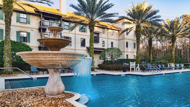 A swimming pool with a tiered fountain, surrounded by palm trees and a building with balconies. - 5201 luxury condo-balcony w/ close up water views-sleeps 6-pool/hot tub (Saint Augustine)