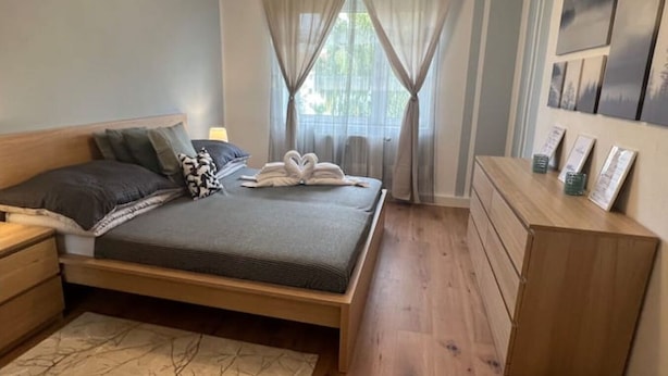 Ein Schlafzimmer mit einem Bett, Nachttischen, einem Schminktisch und einem Fenster mit Vorhängen.