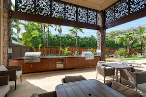 Enjoy al fresco dining in this inviting outdoor kitchen area, featuring a grill station and comfortable wicker furniture.
