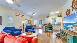 A spacious living area with a large flat-screen TV, a ceiling fan, and a view of the ocean through a large window. - Tagged Out Canal Front, Dock 3 bedroom 2 bath (St. George Island)