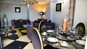 Een eethoek met een zwart en goud gedekte tafel, een bank op de achtergrond en een kroonluchter.