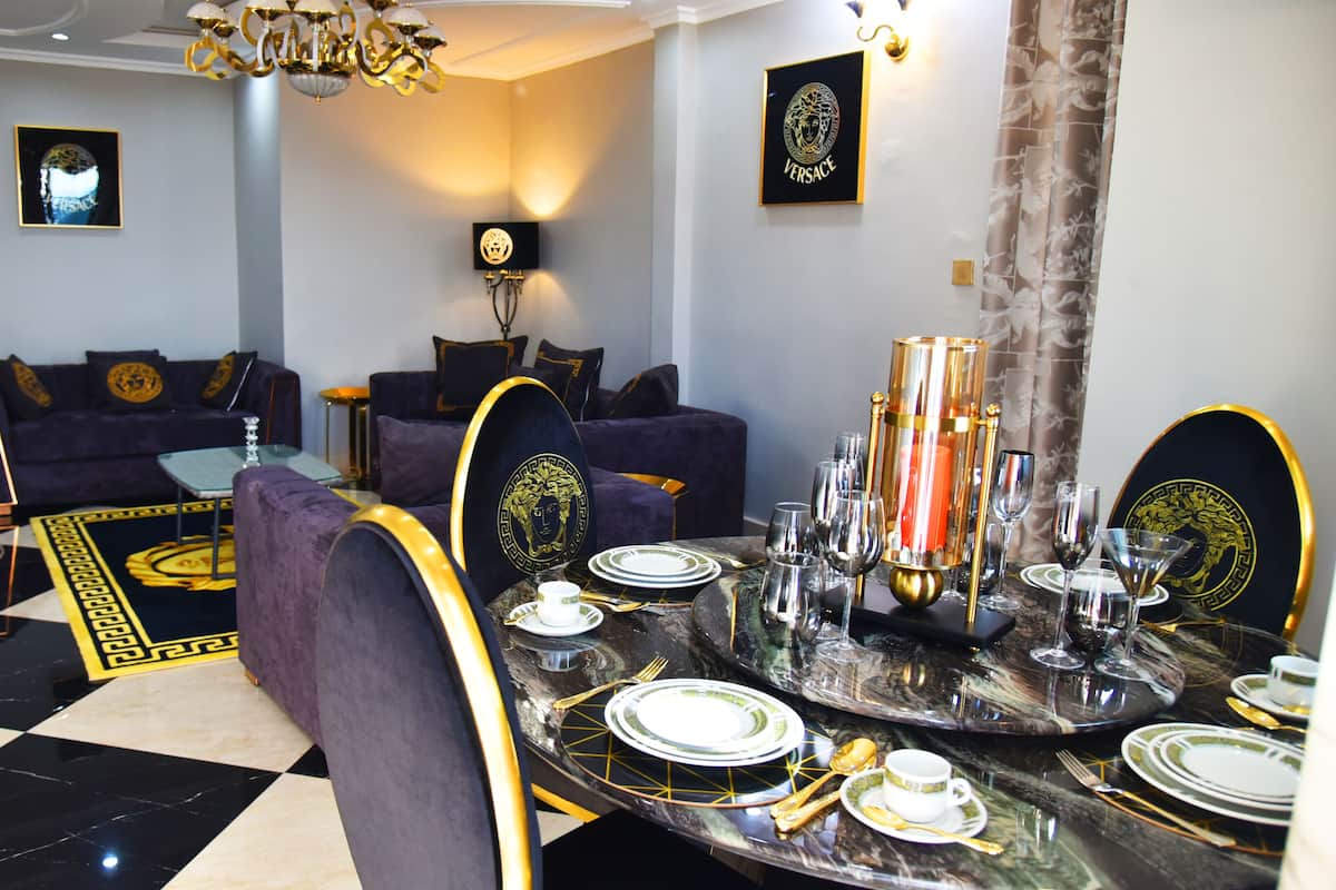 A dining area with a black and gold table set, a sofa in the background, and a chandelier.