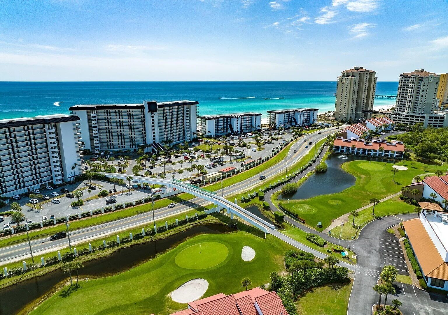 A coastal hotel complex with multiple high-rise buildings, a golf course, and a bridge connecting different areas.
