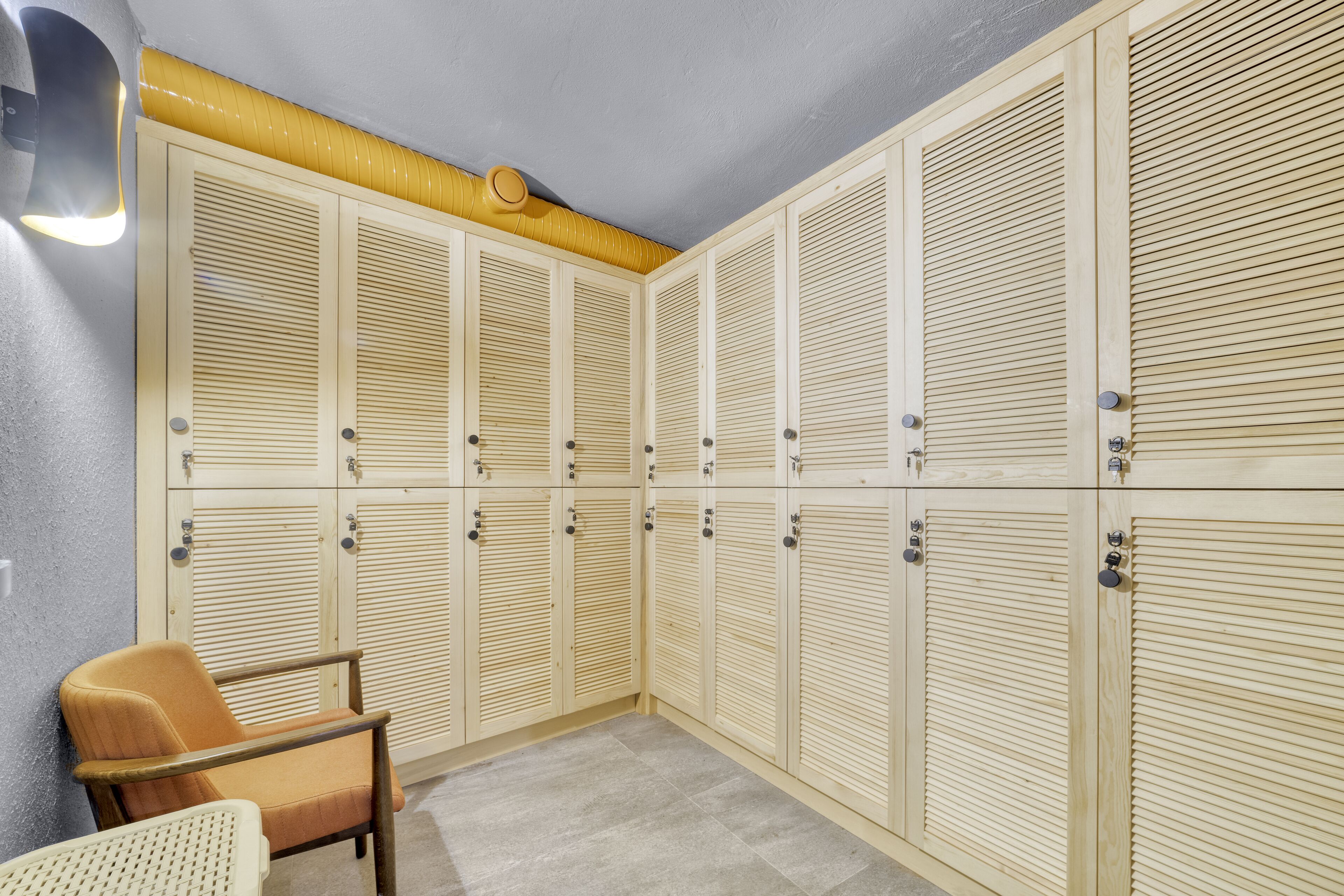 A row of wooden lockers with a light fixture above them and a chair to the left.