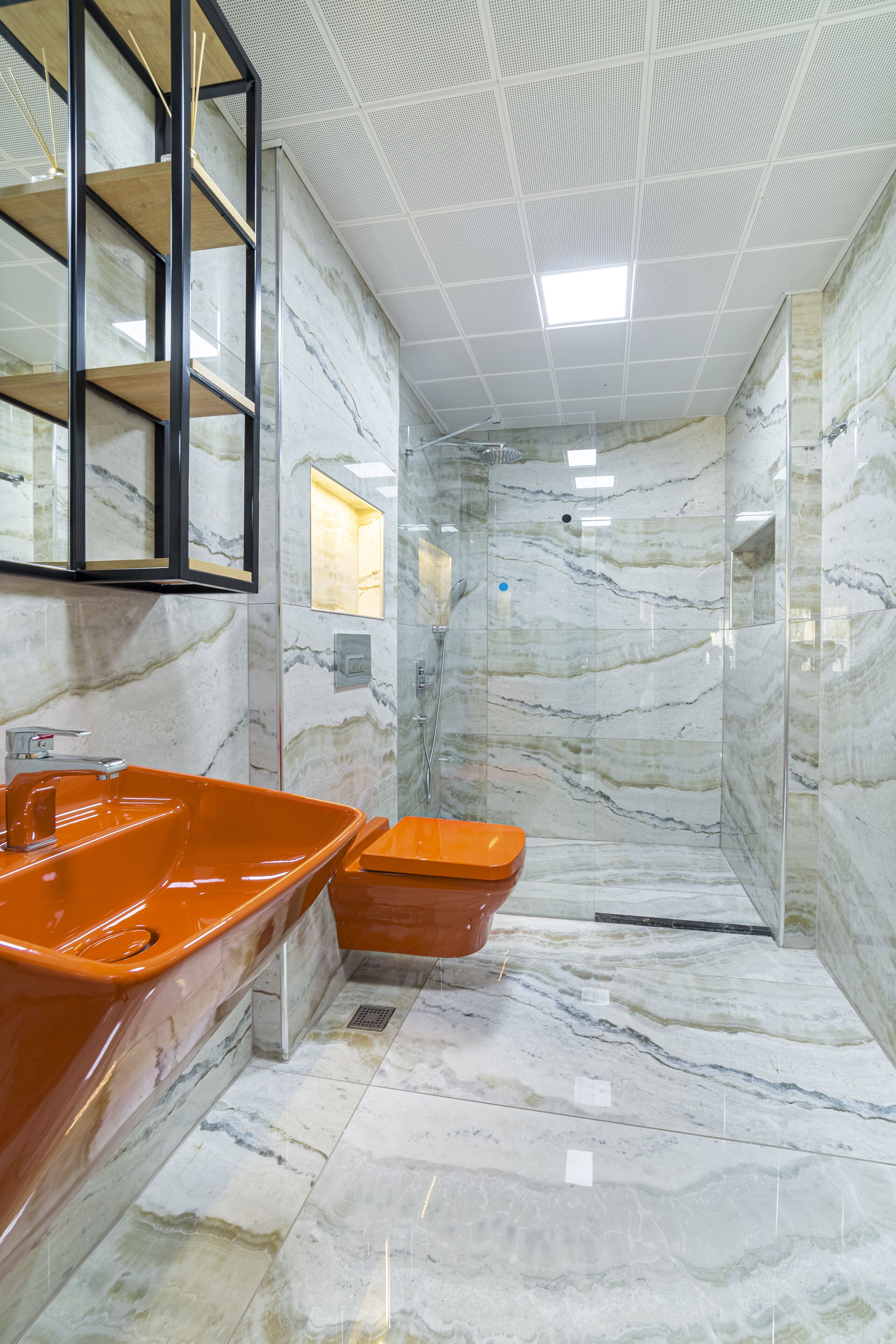 A modern bathroom with a marble floor, a large orange sink, and a shower area.