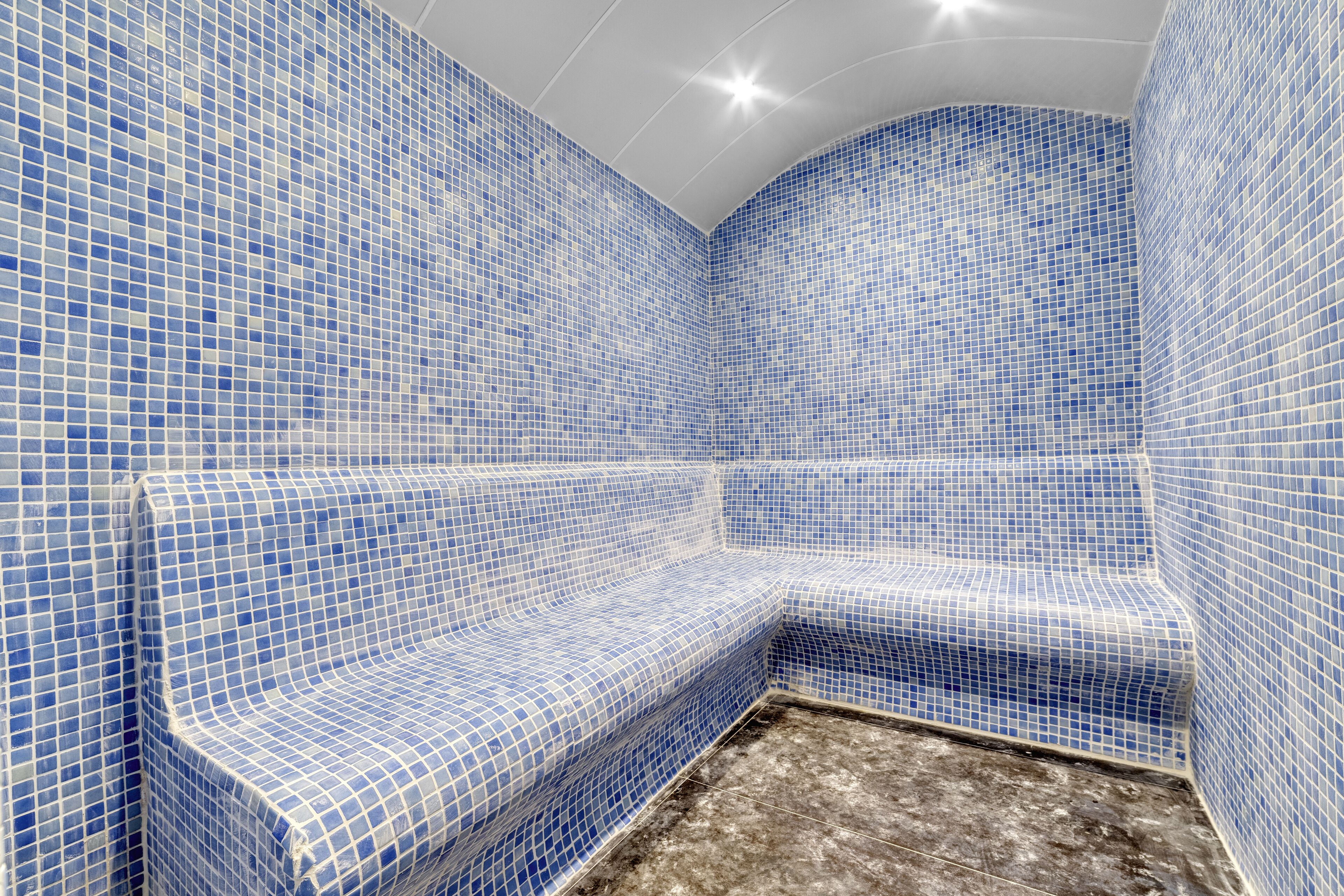 Un baño con mosaicos azules en las paredes y el suelo, un banco y zona de ducha.