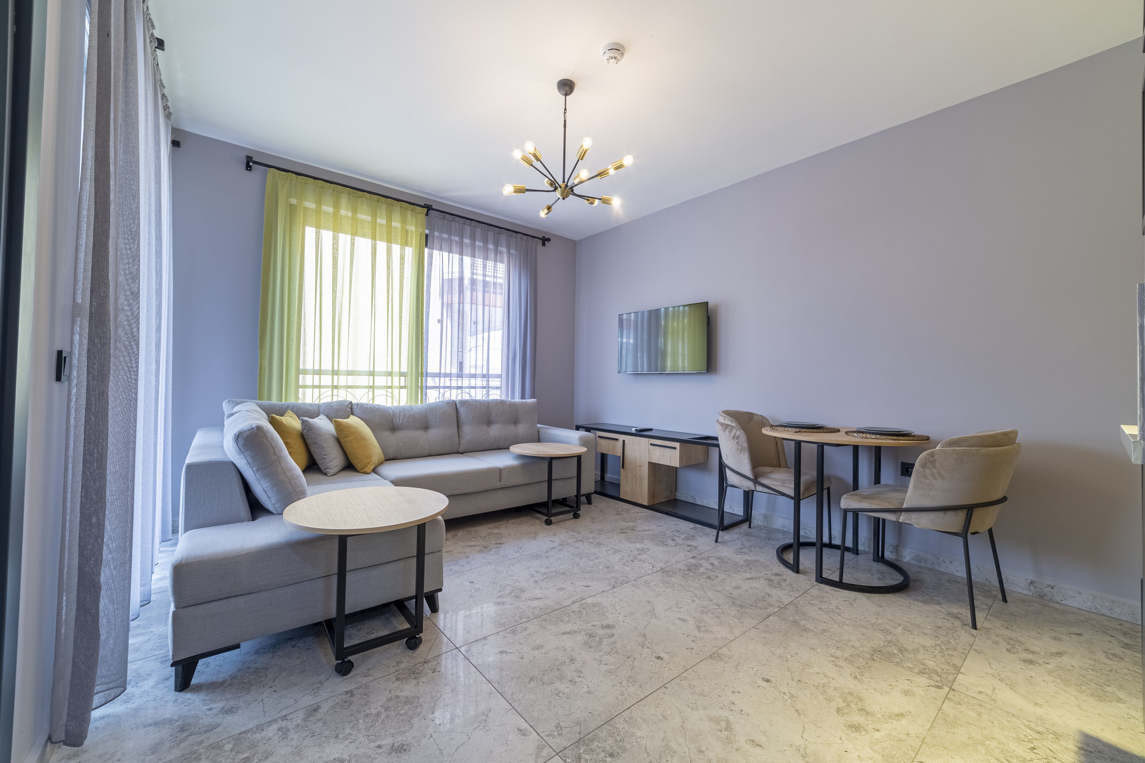 A modern living room with a grey sectional sofa, two round tables, and a desk with chairs.