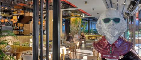 Interior de un restaurante con barra, mesas y una estatua de una figura con chaqueta roja.