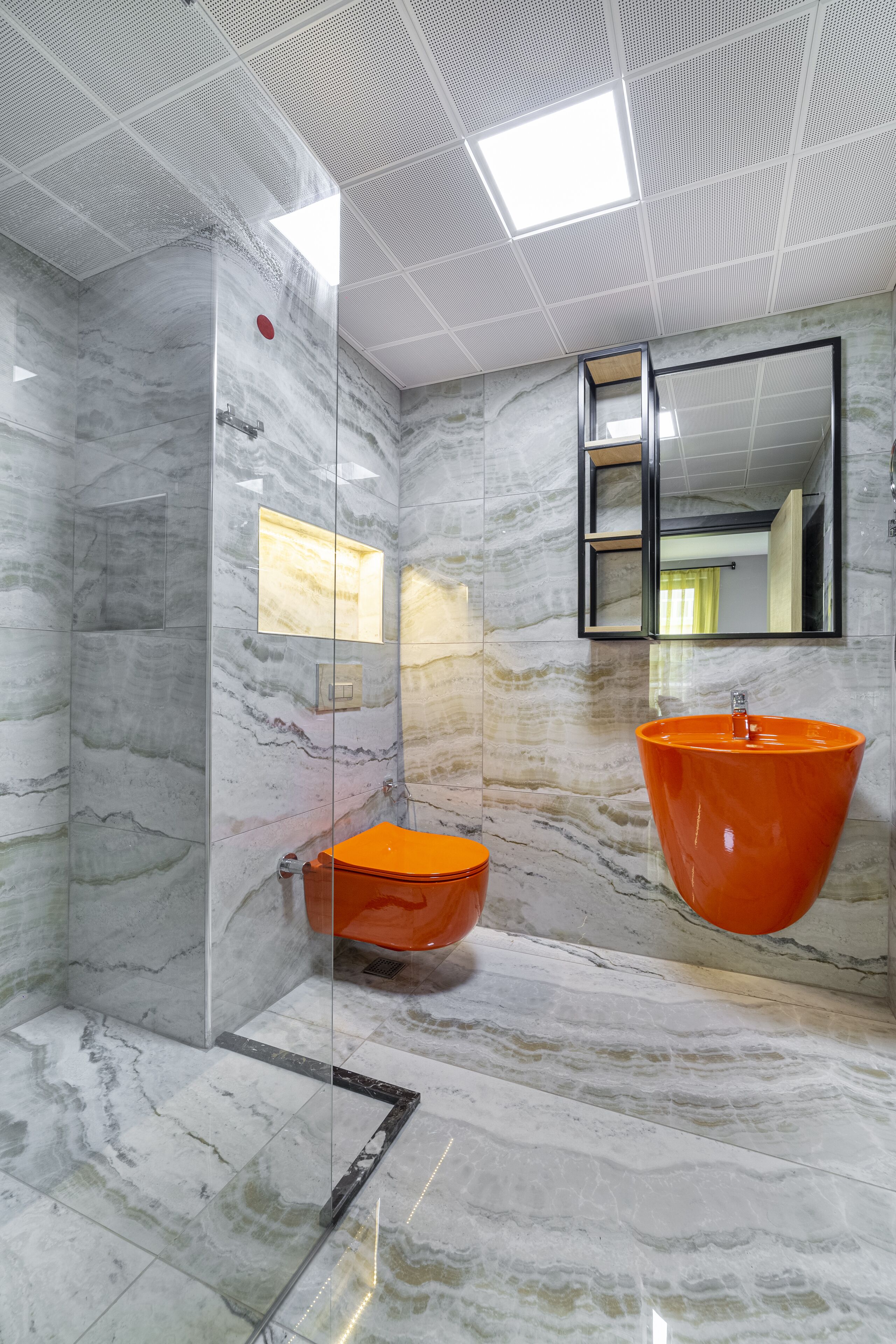Une salle de bain moderne avec une douche à l’italienne en verre, un sol en marbre et un grand lavabo orange.