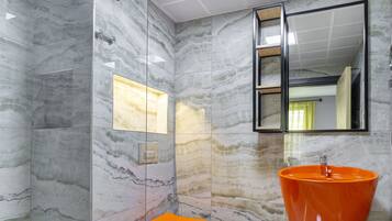 Une salle de bain moderne avec une douche à l’italienne en verre, un sol en marbre et un grand lavabo orange.