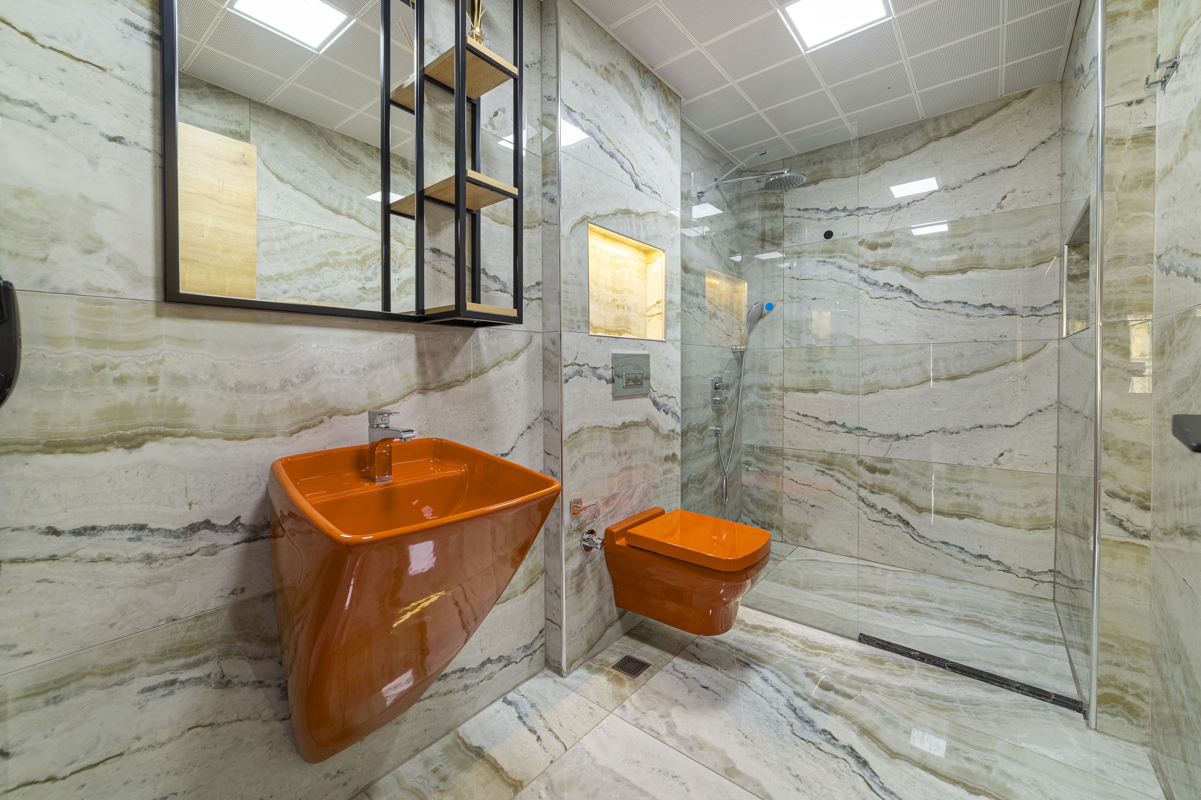 A bathroom with marble walls, a glass-enclosed shower, and a large mirror with a gold frame.