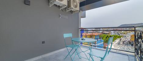 Un balcon doté de deux unités de climatisation, d’une petite table avec des chaises et d’où l’on peut admirer un bâtiment aux couleurs vives en arrière-plan.