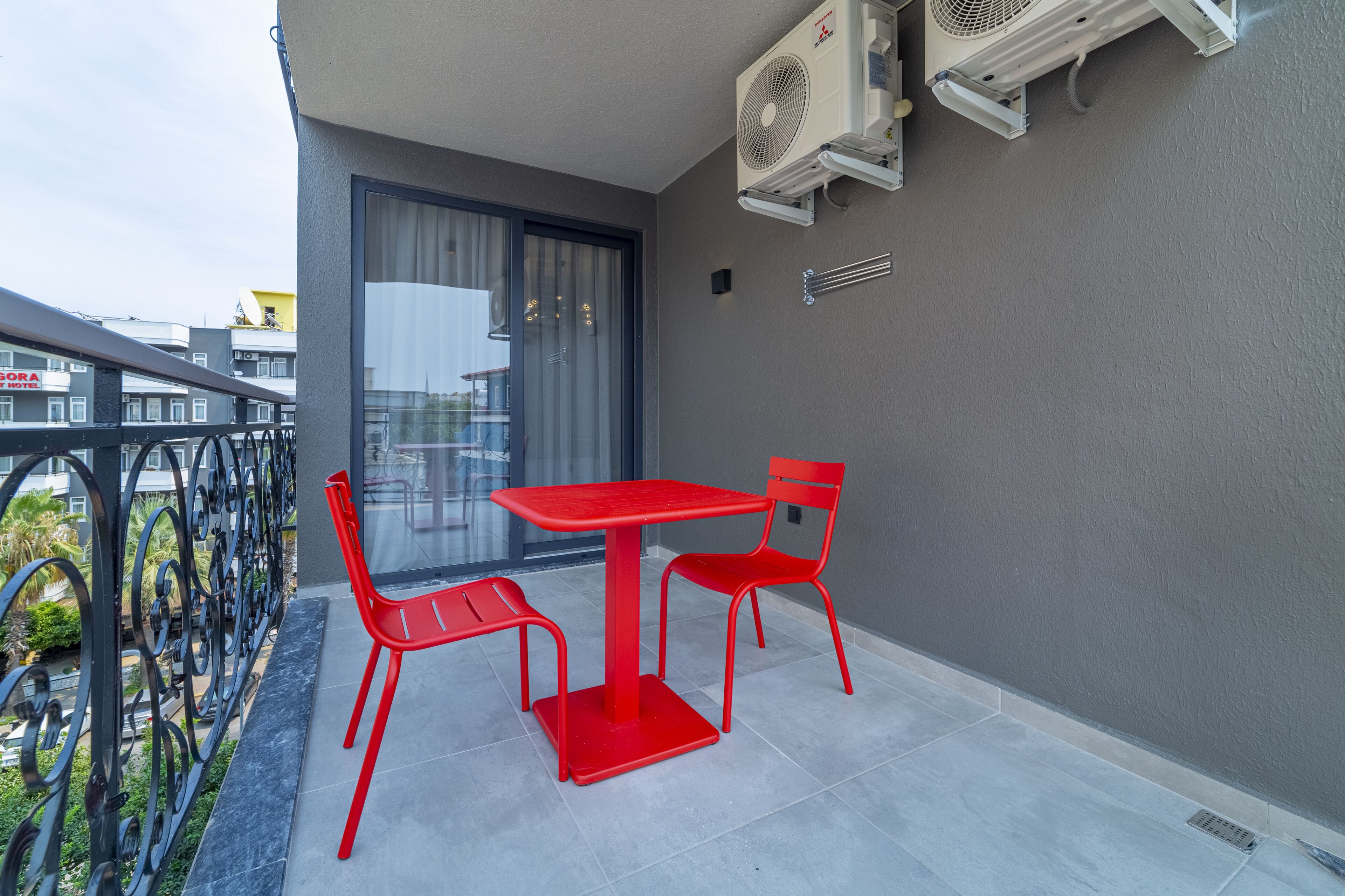 A balcony with a red table and chairs, air conditioning units, and a view of the city.