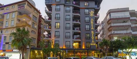 Un hotel de varios pisos con balcones, un cartel que dice 'Larsen's Suit Hotel' y varios coches aparcados delante.