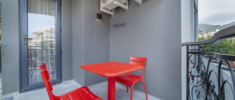 A balcony with a red table and chairs, air conditioning units, and a view of the city.