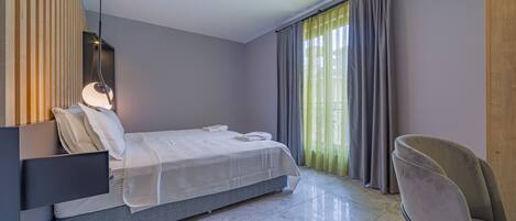 A modern bedroom with a bed, a chair, a bedside table, and a window with curtains.