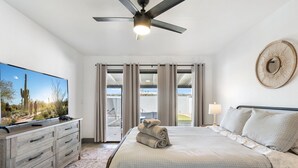 A hotel room with a large bed, a flat-screen TV, a ceiling fan, a view through the window, and a decorative wall piece. - Home in the Heart of Glendale (Glendale)