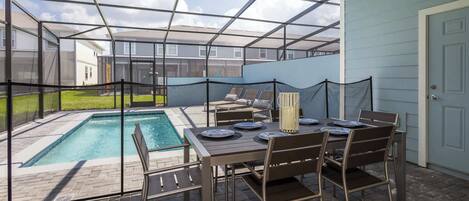 A covered patio with a pool, outdoor seating, and a table set for dining.