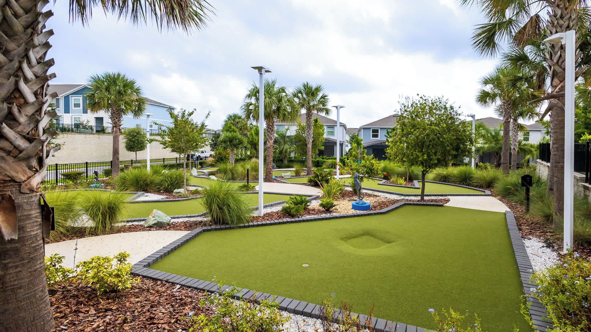 A golf course with a putting green, surrounded by palm trees and residential buildings.