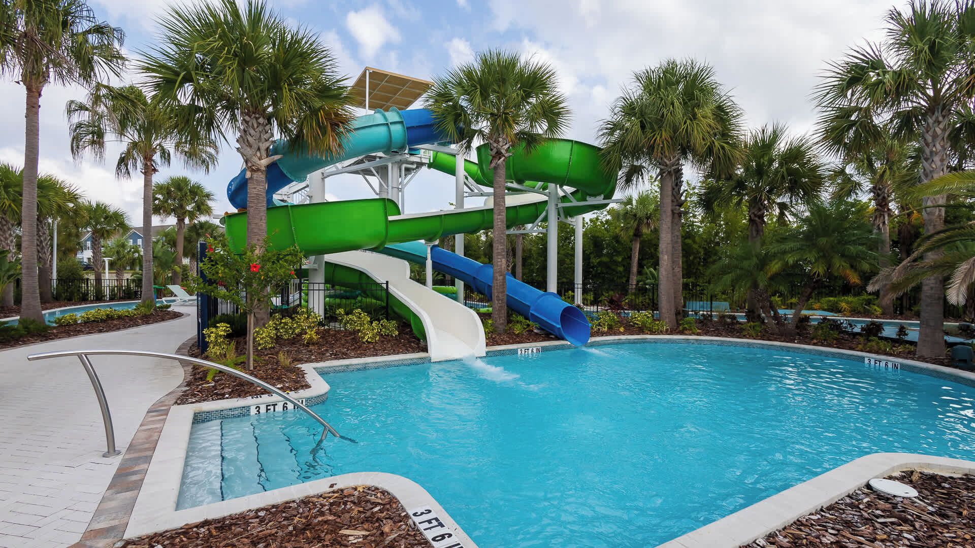 A pool with a water slide, palm trees, and a clear sky.