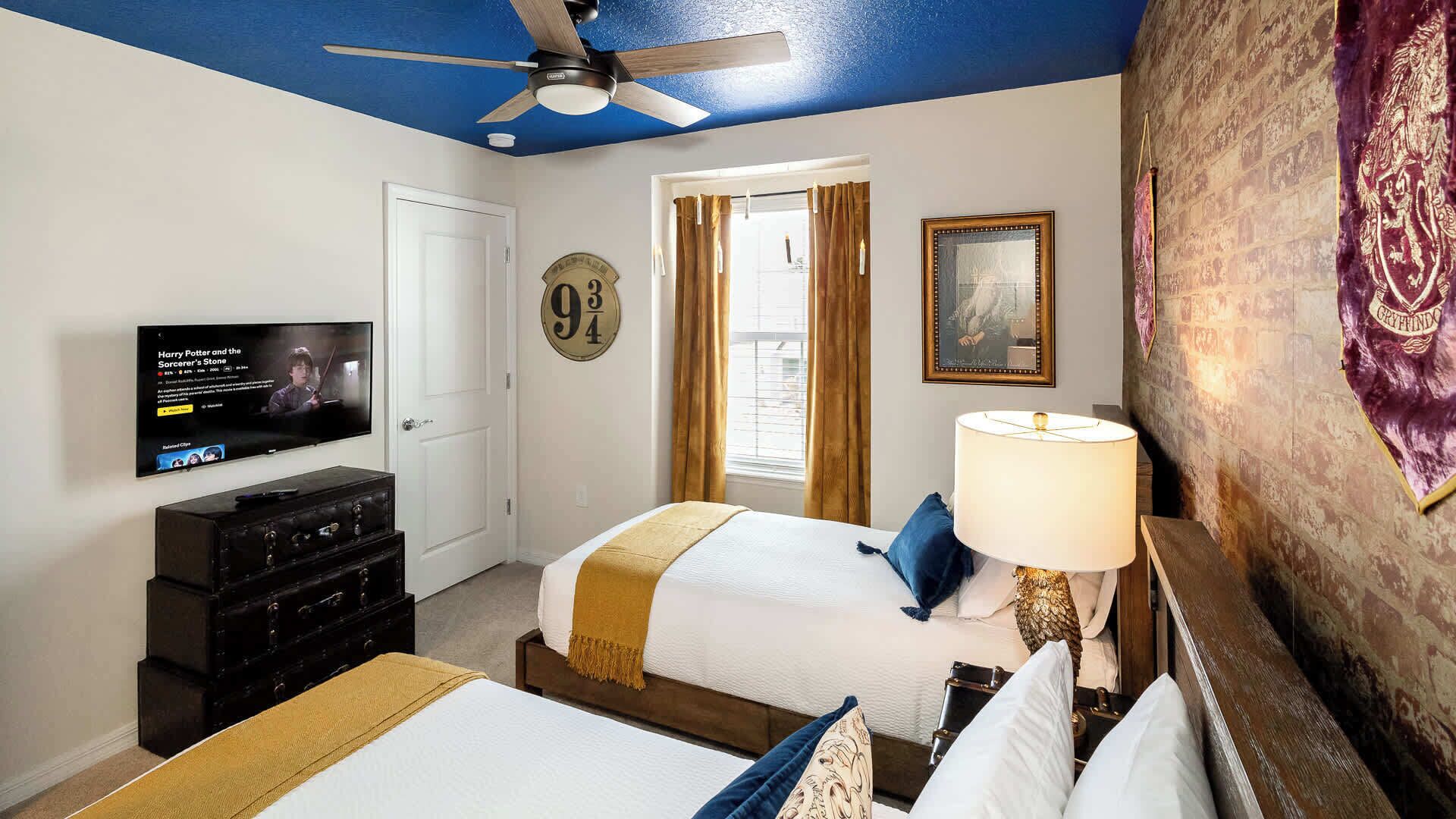 A hotel room with a bed, a television, a ceiling fan, and a wall with a Gryffindor banner.