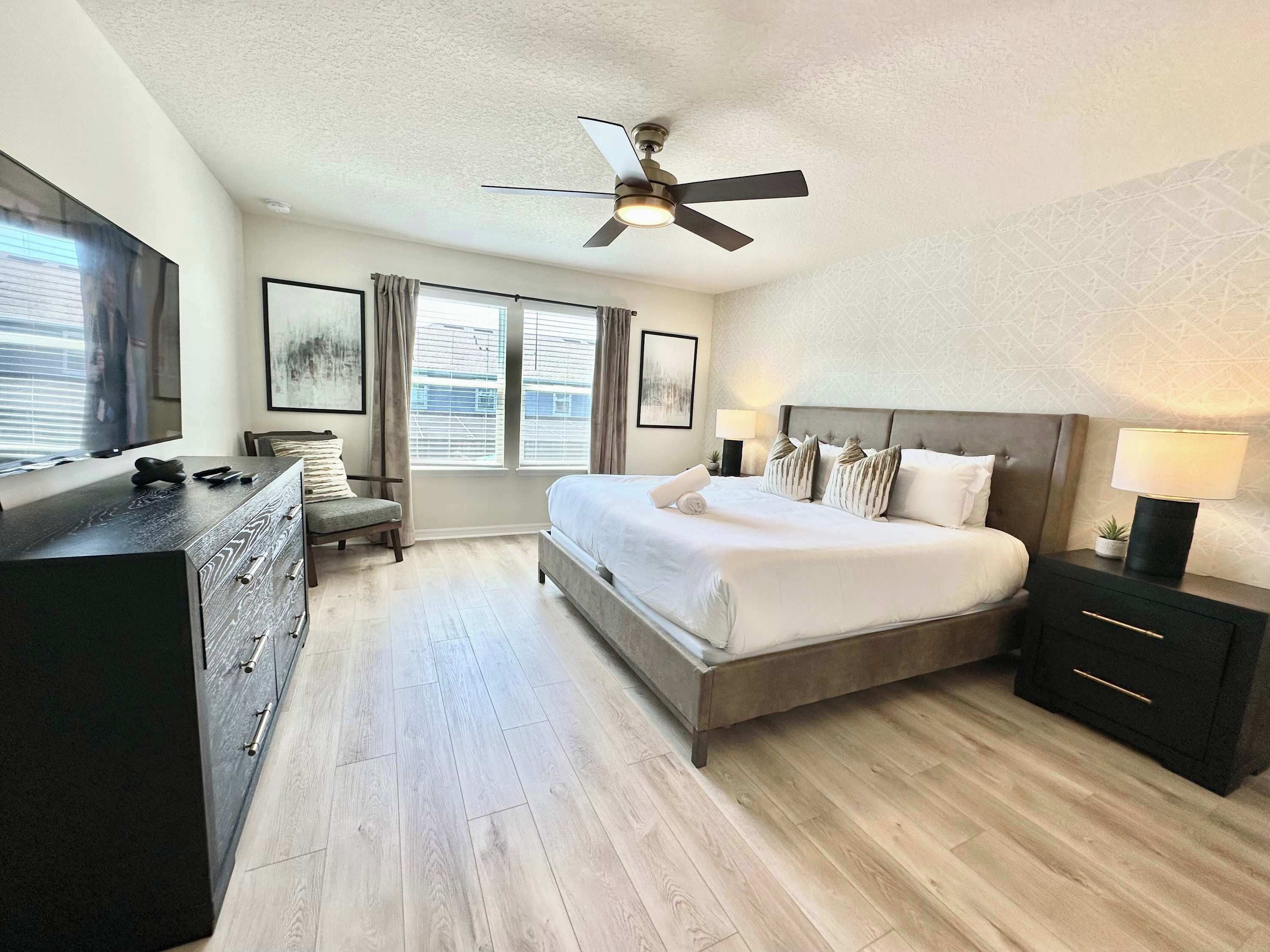 Une chambre d’hôtel moderne avec un grand lit, un ventilateur de plafond, une commode et un téléviseur.