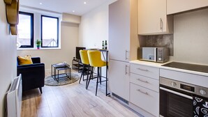 A modern kitchen with a microwave, oven, and dining area with yellow chairs. - Hybrid Resi - Cheam  (Sutton)