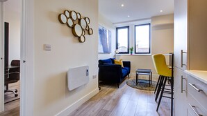 A modern living room with a blue sofa, a yellow chair, and a dining area with a table and chairs. - Hybrid Resi - Cheam  (Sutton)