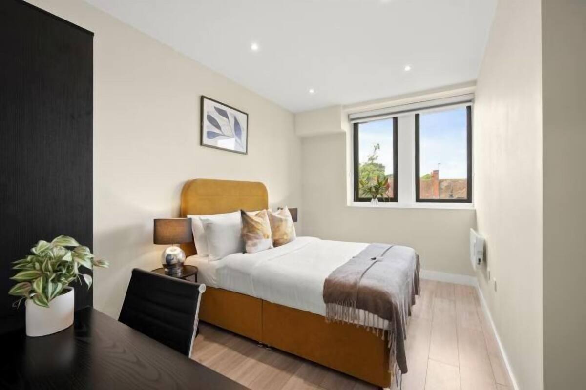A bedroom with a bed, bedside table, lamp, and a window with a view.