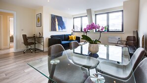 A modern living room with a glass dining table, comfortable seating, a blue sofa, and large windows. - Hybrid Resi - Cheam  (Sutton)