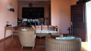 Un espacio de sala acogedor con mobiliario de mimbre, una mesa de comedor y vista al área de comedor.