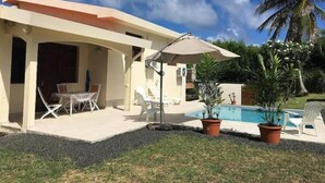 Un espacio al aire libre techado con piscina, sillas de descanso y una mesa.