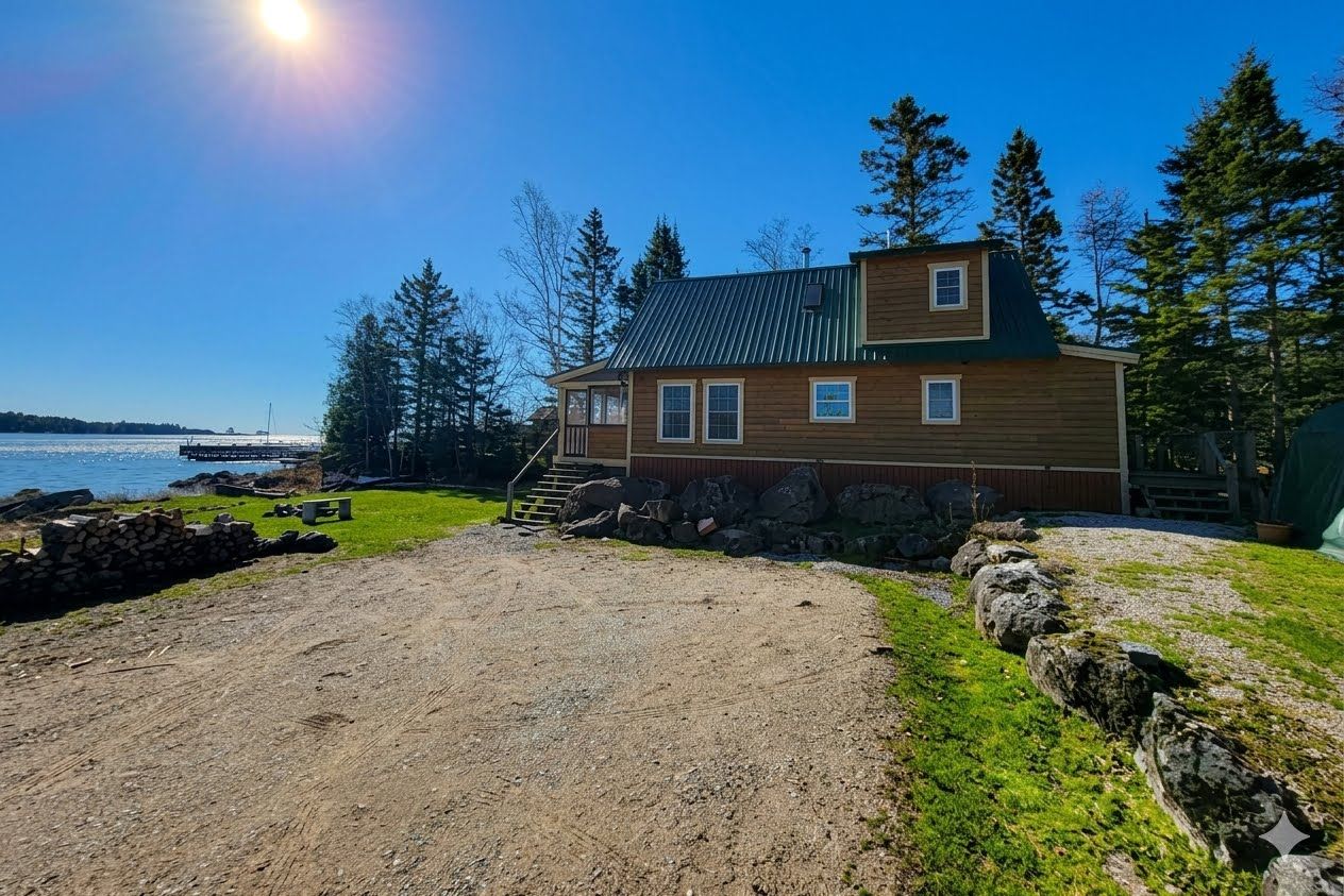 A two-story wooden cabin with a metal roof, a stone wall, and a gravel path leading to the entrance.