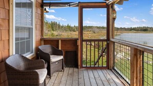 Terraza de madera con sillas de mimbre y vista a un lago.