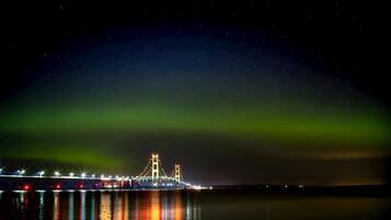 A bridge with lights reflecting on water, under a night sky with visible stars and green aurora.