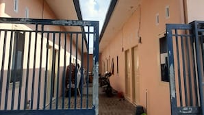 A corridor with a tiled floor, a metal gate, and a person walking. - Hotel O Modena Homestay Syariah Near SD Negeri 101798 Deli Tua (Medan)