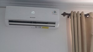 A wall-mounted air conditioning unit with a digital display, labeled "SHARP," and a yellow maintenance tag. - Hotel O Modena Homestay Syariah Near SD Negeri 101798 Deli Tua (Medan)