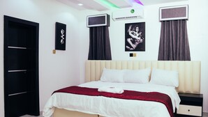 Quarto bem arrumado com cama, mesas de cabeceira, guarda-roupa e televisão na parede.