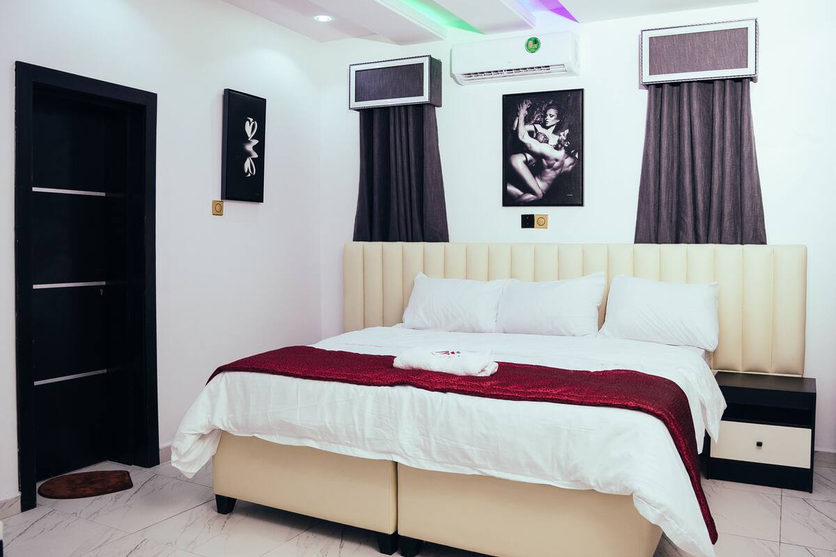 Een keurig opgemaakt slaapkamer met een bed, nachtkastjes, een kledingkast en een aan de muur bevestigde televisie.