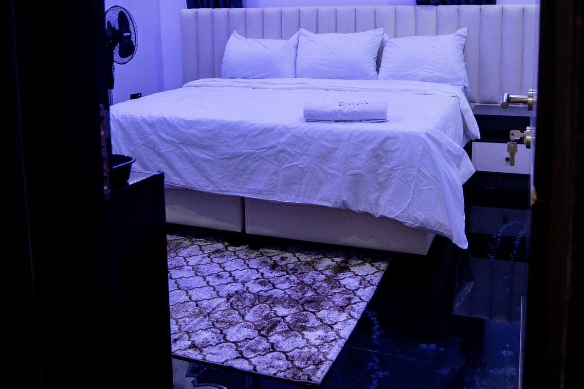 Een moderne slaapkamer met een bed, nachtkastjes, een wandairconditioner en een plafondlamp.