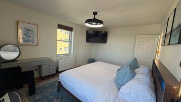 A bedroom with a bed, a desk, a chair, a radiator, a window, and a television.