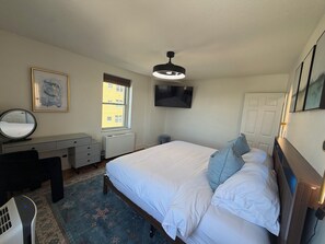 A bedroom with a bed, a desk, a chair, a radiator, a window, and a television. - Come enjoy a cozy, spacious high-rise condo with breathtaking sunset views. (Atlanta)