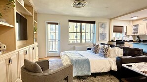 A modern living room with a sofa, a coffee table, a bed, and a built-in kitchen area. - Come enjoy a cozy, spacious high-rise condo with breathtaking sunset views. (Atlanta)