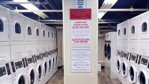 A laundry facility with rows of washing machines, a sign instructing to wear a face mask, and guidelines for using the machines. - Come enjoy a cozy, spacious high-rise condo with breathtaking sunset views. (Atlanta)